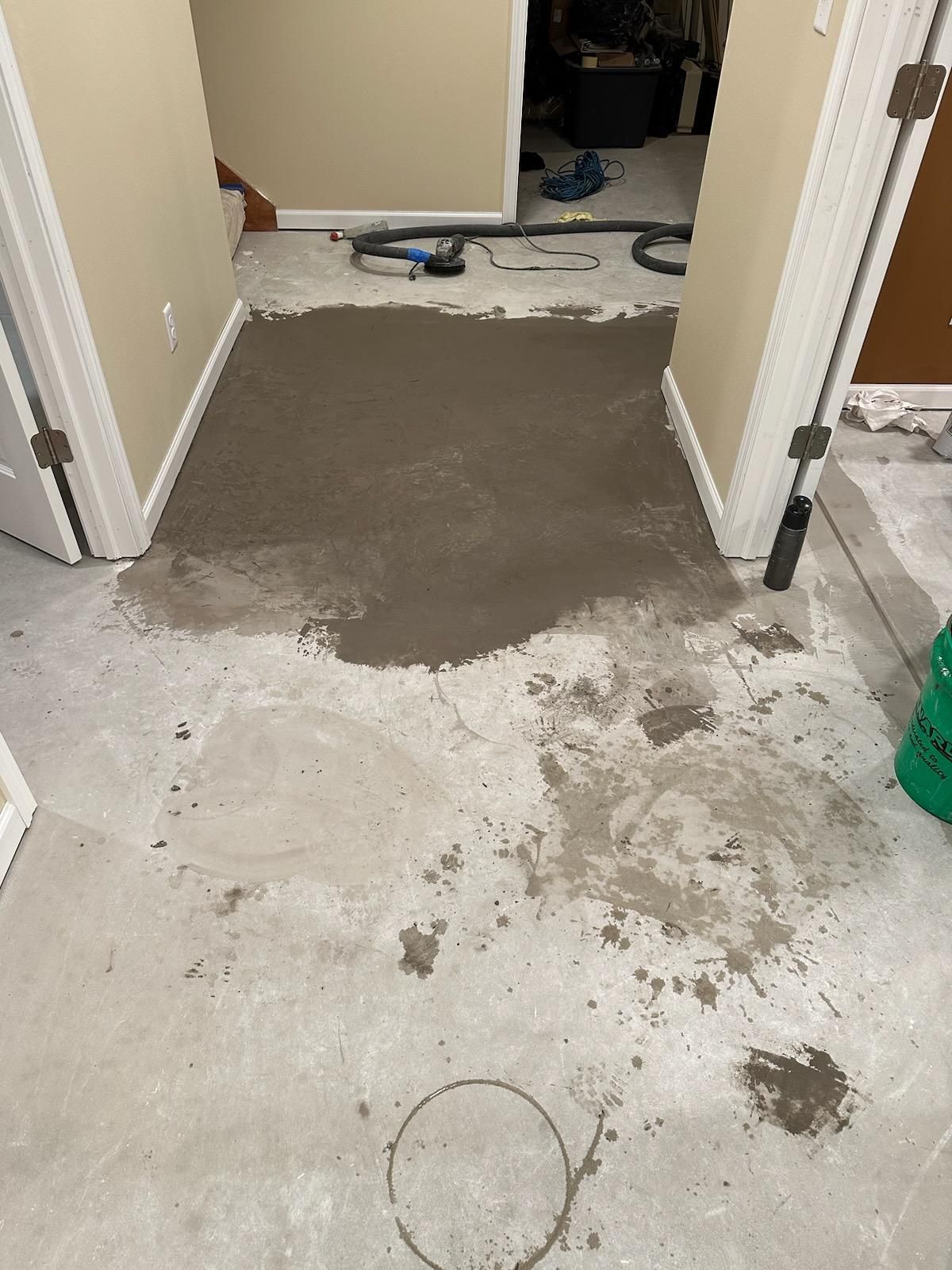 Partially repaired hallway floor with gray patching compound and scattered debris leading into a room