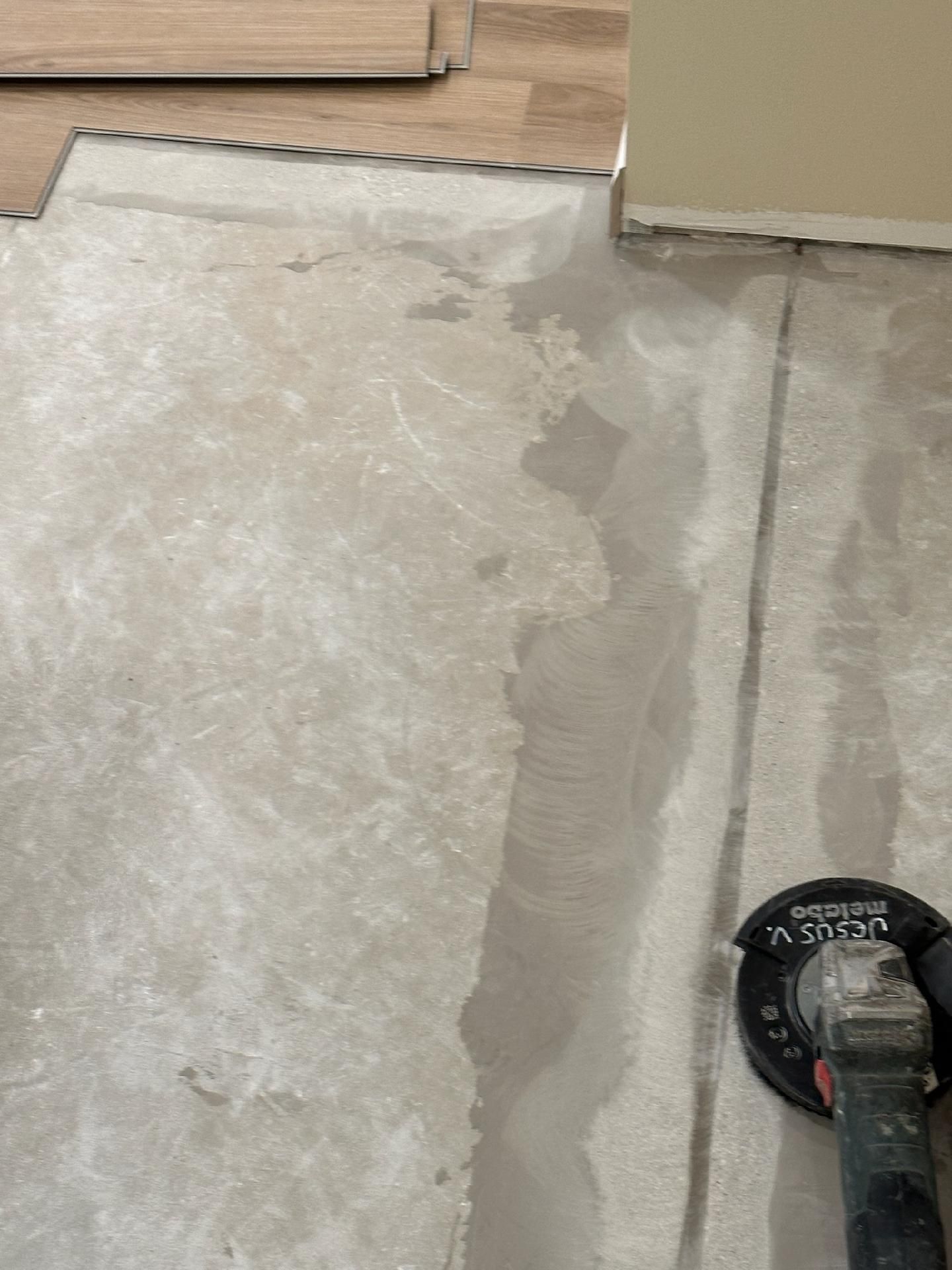 Concrete floor patch next to cardboard boxes, with a grinding tool at lower right.