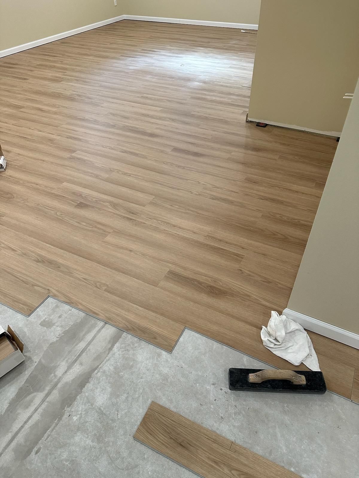 Empty room with light wood flooring being installed, showing tools and unfinished edges.