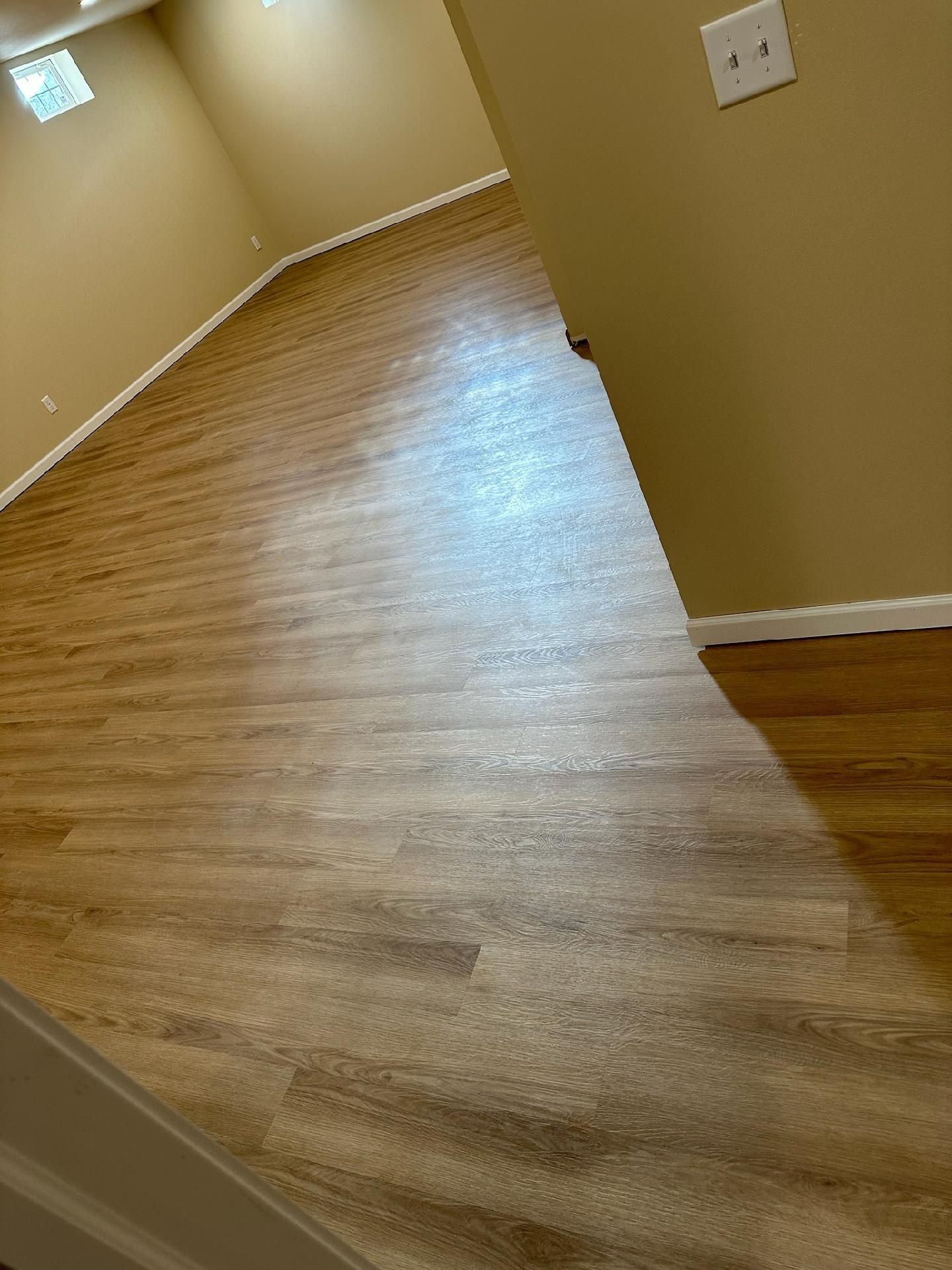 Empty beige room with wood laminate flooring and a white wall outlet, viewed from a doorway.