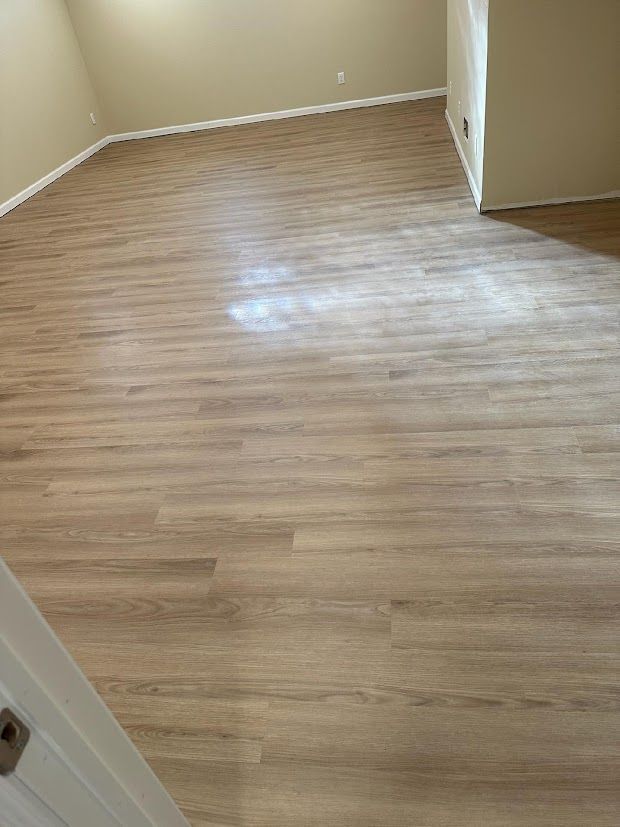 Empty beige room with light wood-look flooring and white baseboards