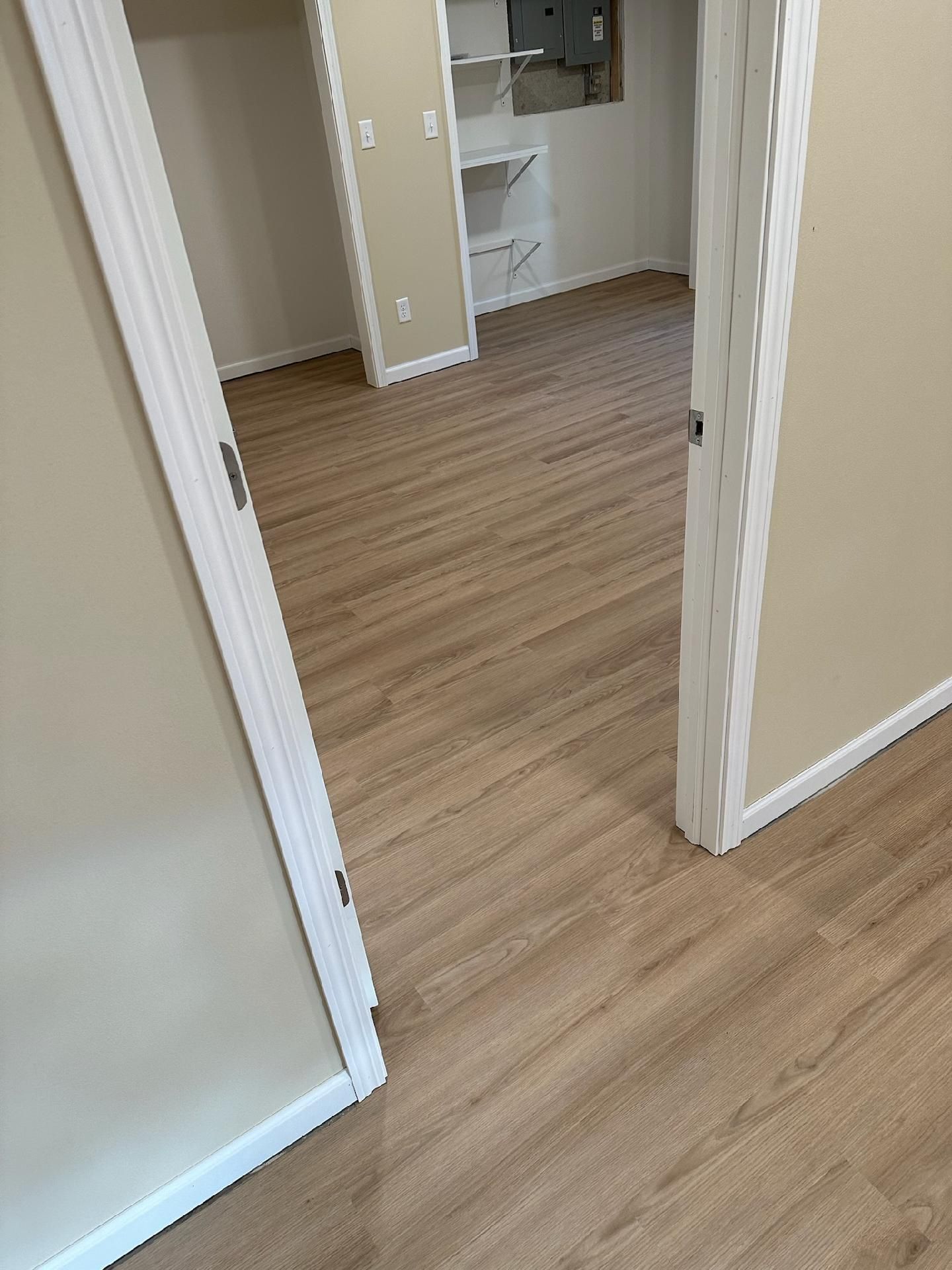Empty hallway with wood flooring and open doorways leading to a closet or bathroom area