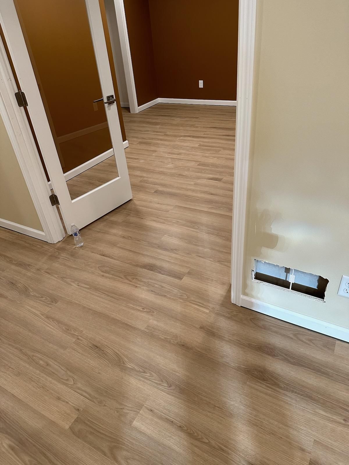 Empty room with wood-look flooring, brown walls, and an open white door.
