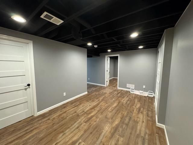 Empty finished basement room with gray walls, wood-look floor, and black ceiling lights