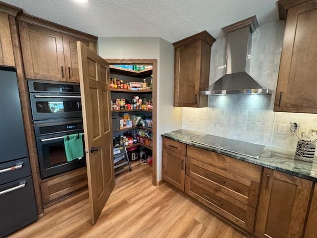 Modern kitchen with wood cabinets, stainless range hood, and open pantry door revealing stocked shelves