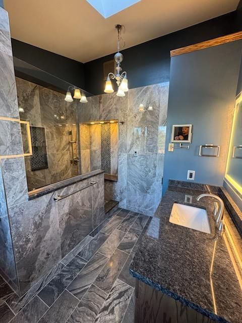 Modern tiled shower with gray marble walls, glass enclosure, and hanging pendant lights