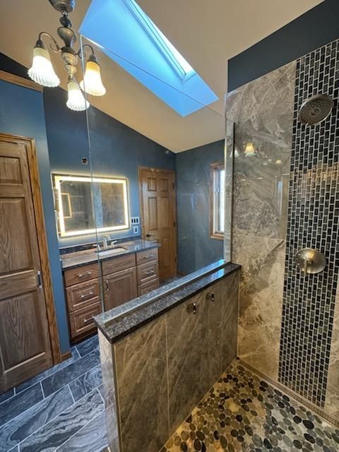 Luxury bathroom with skylight, vanity mirror, wood cabinets, and tiled walk-in shower