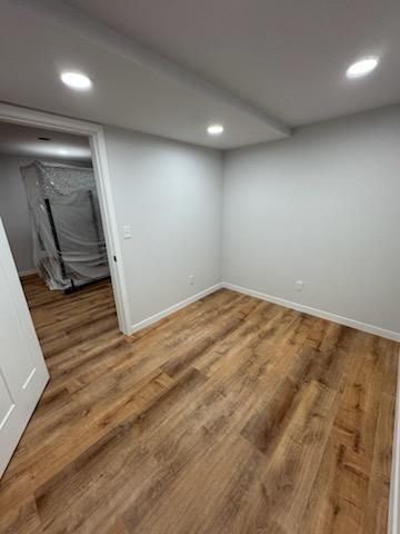 Empty white room with wood flooring and recessed ceiling lights, doorway to a covered area.