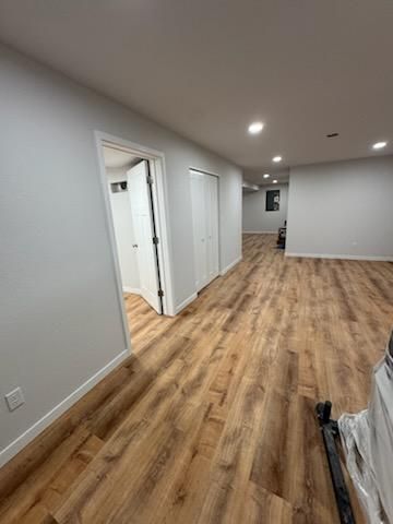 Empty hallway with wood floors, white walls, recessed lights, and open doorways in a modern interior.