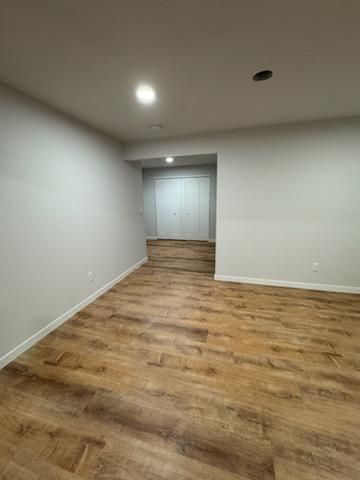 Empty room with wood flooring, white walls, ceiling light, and closed double doors in back.