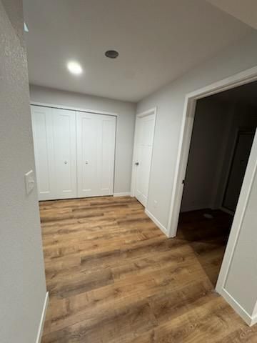 Empty hallway with white closet doors, a closed door, and wood-look flooring.