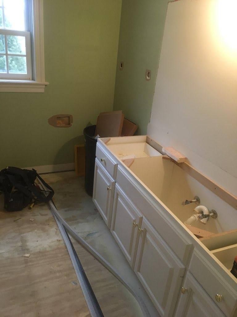 Bathroom renovation with white vanity cabinets, exposed pipes, and tools on the floor.