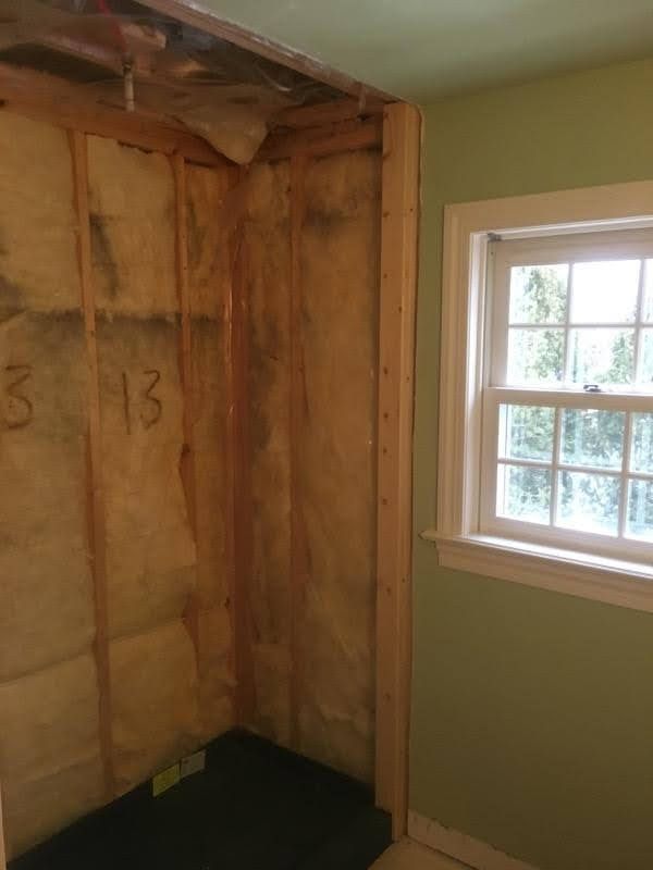 Unfinished room corner with exposed insulation and a window beside a pale green wall.