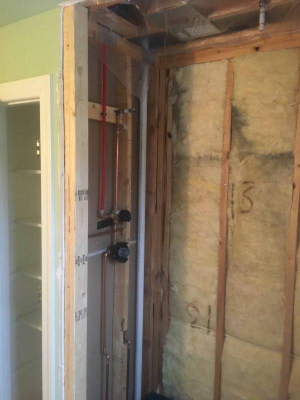 Partially demolished wall exposing studs, insulation, and plumbing pipes in an interior room