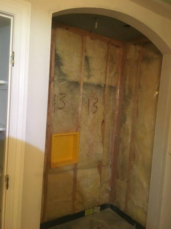 Unfinished doorway under an arch, with exposed insulation and a yellow vent opening in the wall.