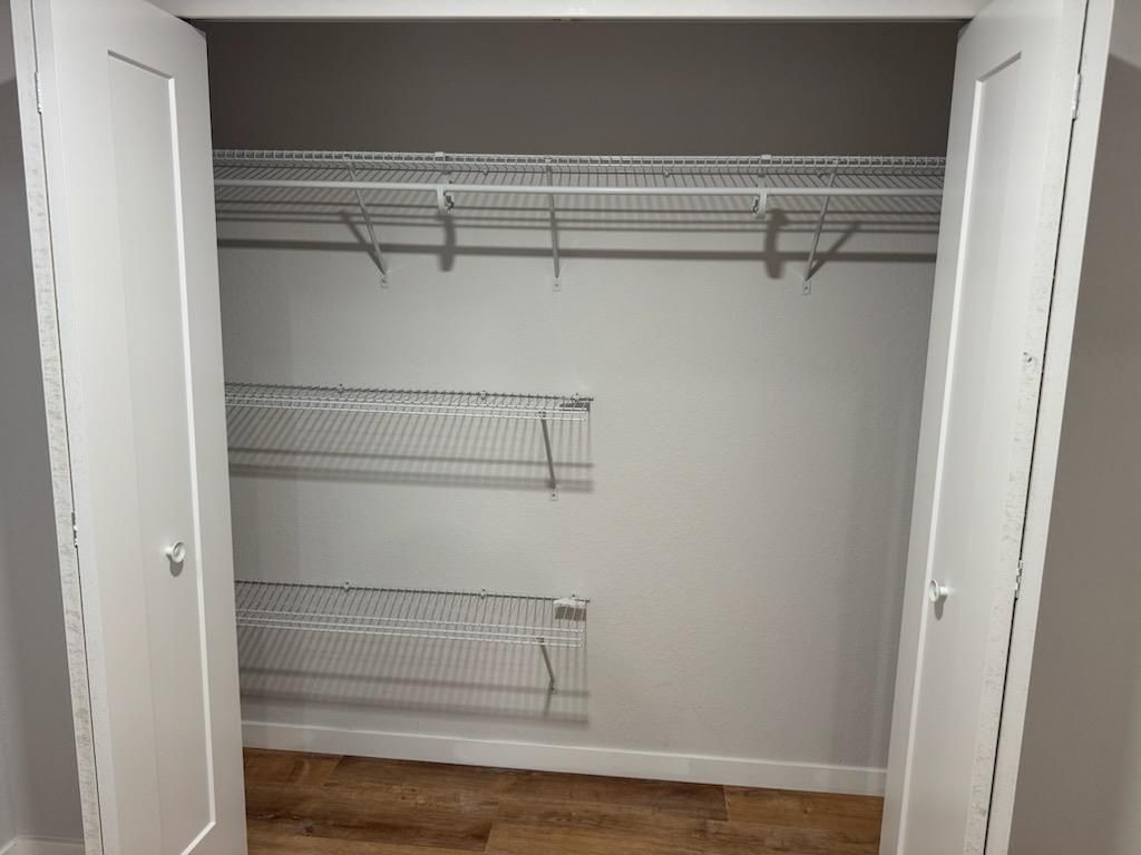 Walk-in closet with white wire shelves and hanging rods, mostly empty with open double doors