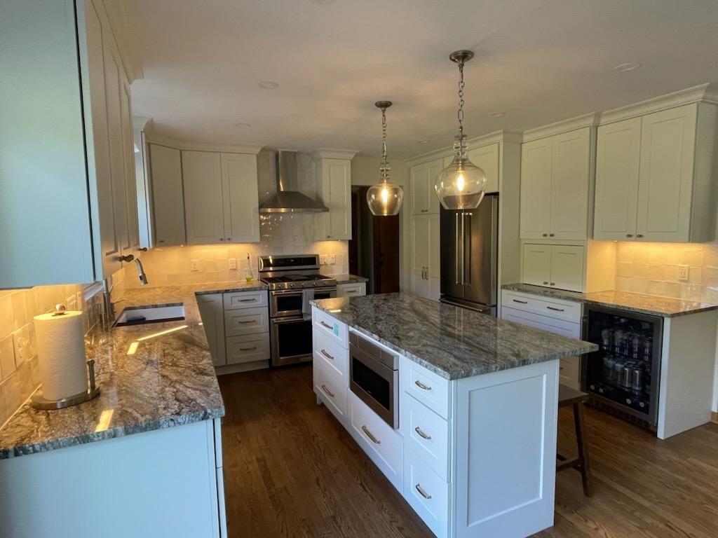 Bright modern kitchen with white cabinets, granite island, pendant lights, and stainless-steel appliances