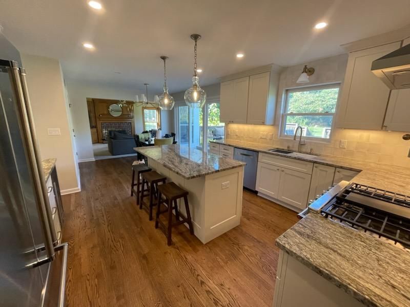 Bright modern kitchen with island, bar stools, granite counters, white cabinets, and hardwood floors.