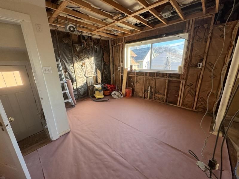 Unfinished room with exposed framing, pink floor covering, and a large window letting in daylight