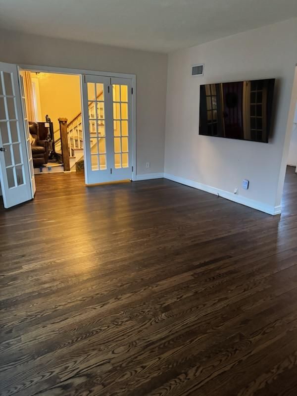 Empty living room with dark wood floors, French doors, and a wall-mounted TV.