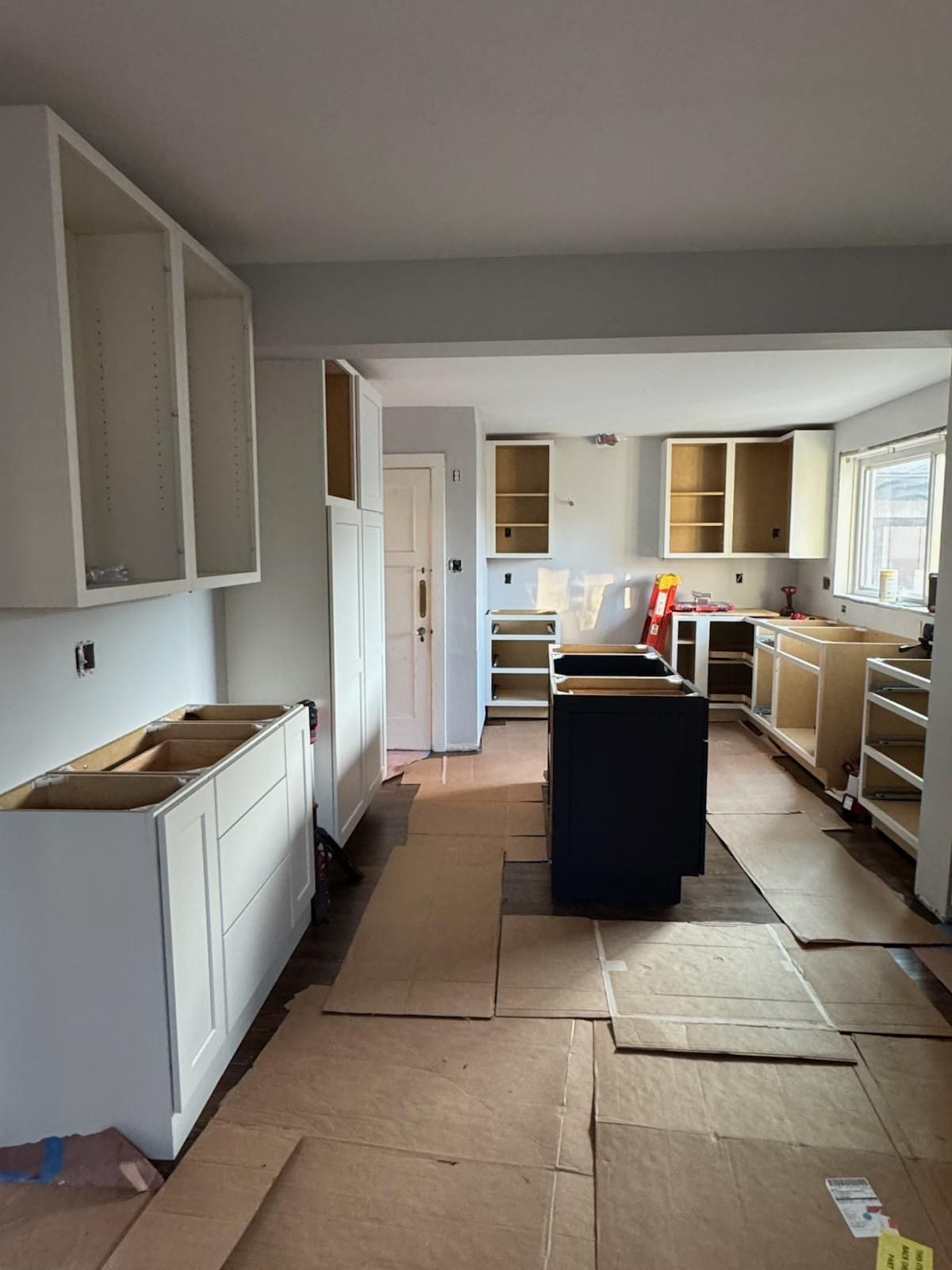 Unfinished kitchen with cardboard-covered floor, white cabinets, and a dark island under renovation