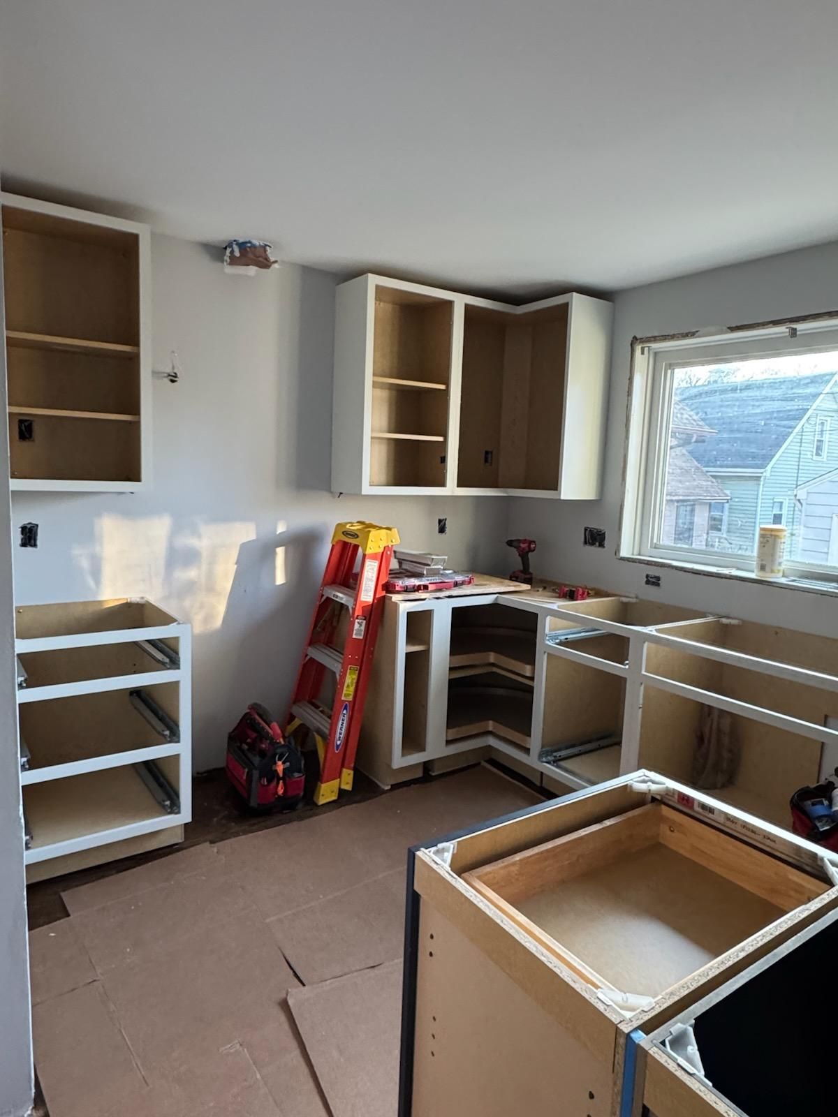 Partially renovated kitchen with unfinished cabinets, tools, and a window letting in daylight