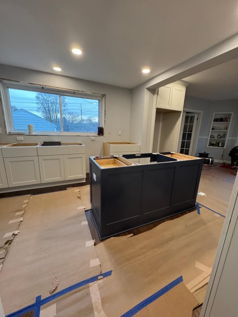 Kitchen renovation in progress with a black island cabinet and taped-off wood flooring.