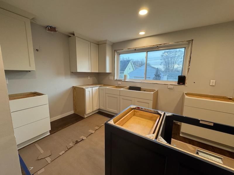 Partially renovated kitchen with white cabinets, unfinished island, and a window overlooking snowy houses