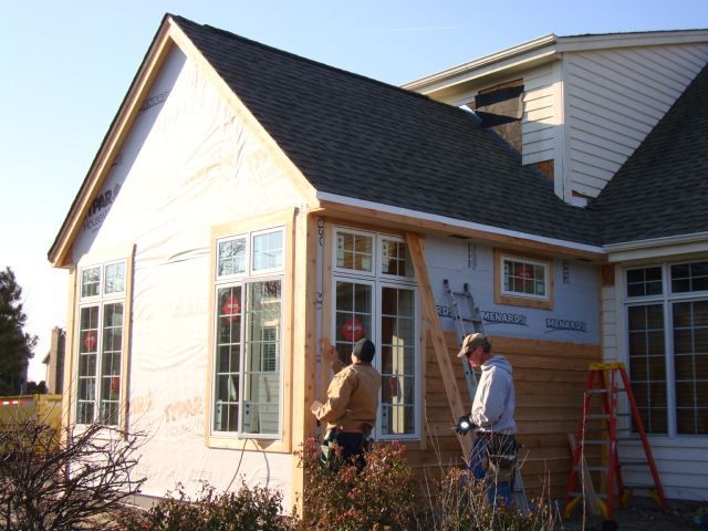 Two workers installing windows on a house exterior with a ladder and tools