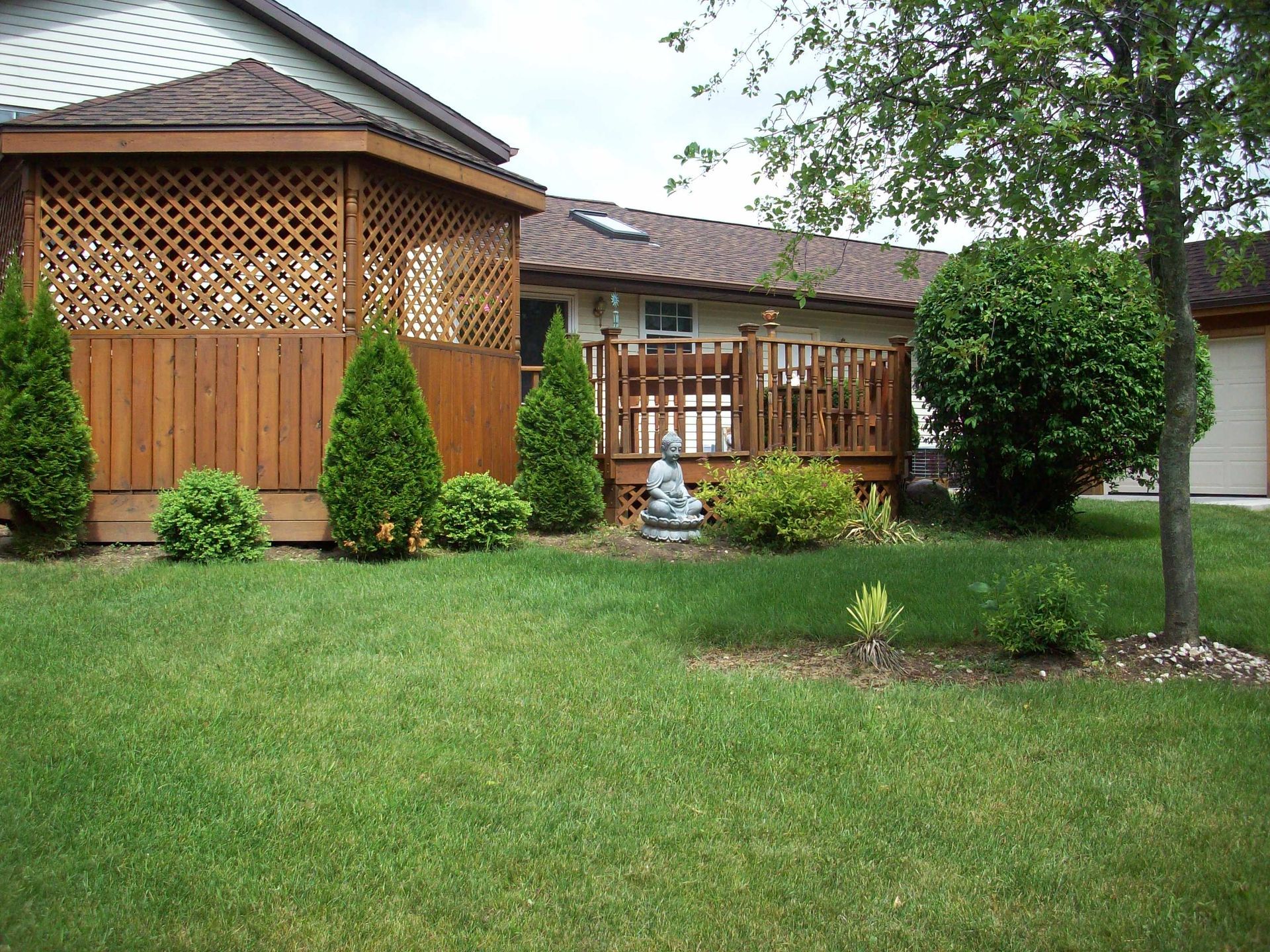 Backyard with green lawn, wooden gazebo, small fountain, and trees beside a house