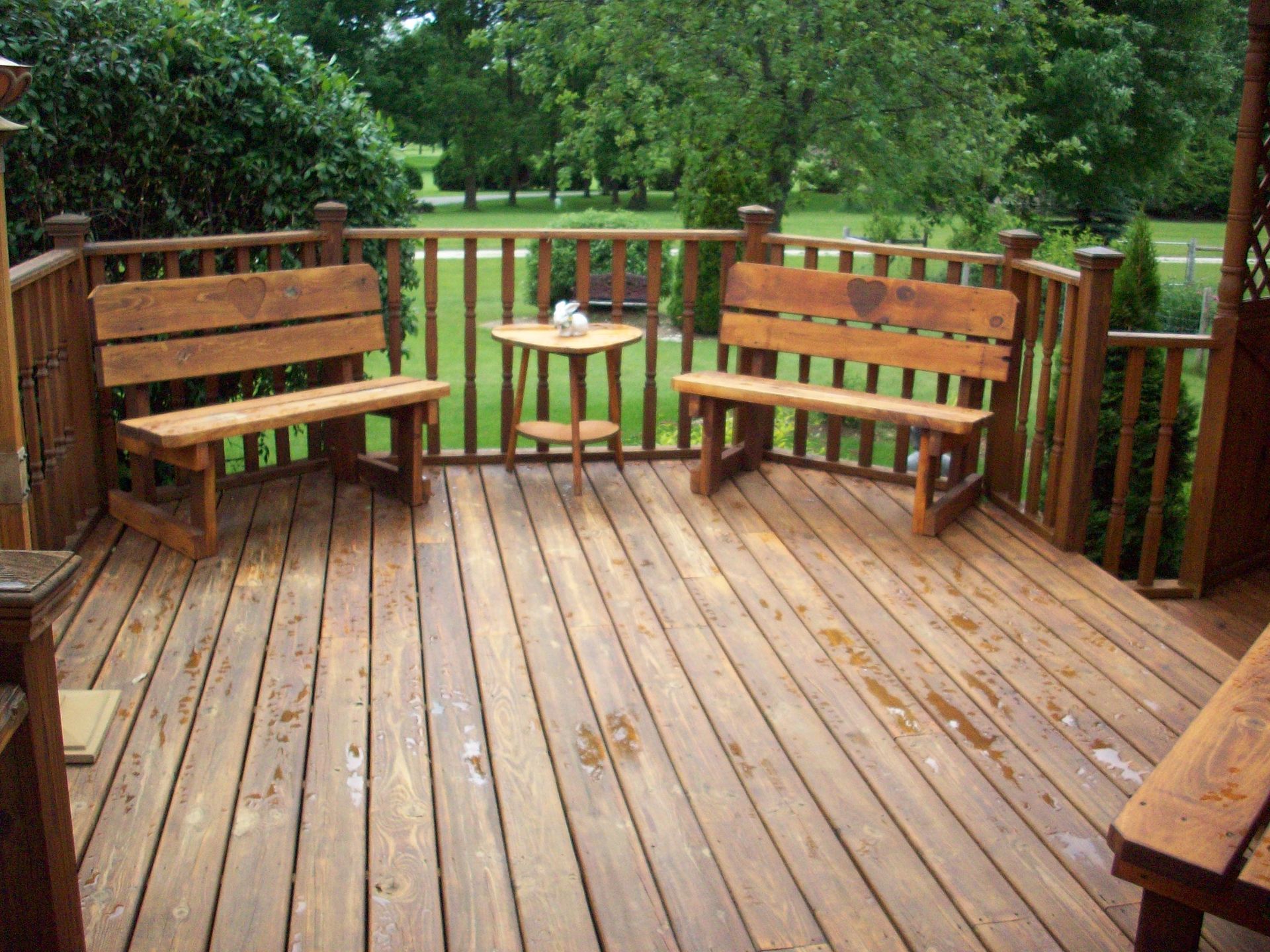 Wooden deck with benches and a small table, surrounded by green trees