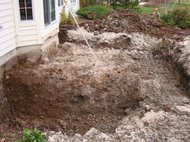 Large backyard excavation beside a house, with exposed soil and a deep hole filling most of the yard