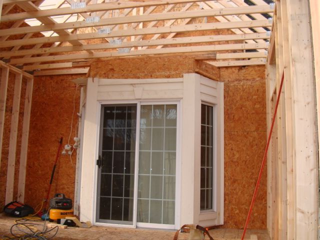 Wood-framed porch under construction with sliding glass doors and exposed brick walls
