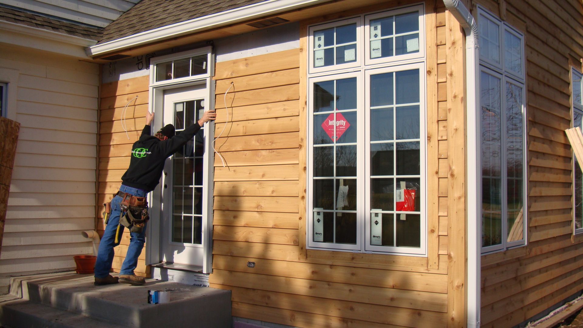 Person working on a white door outside a wooden house with large windows