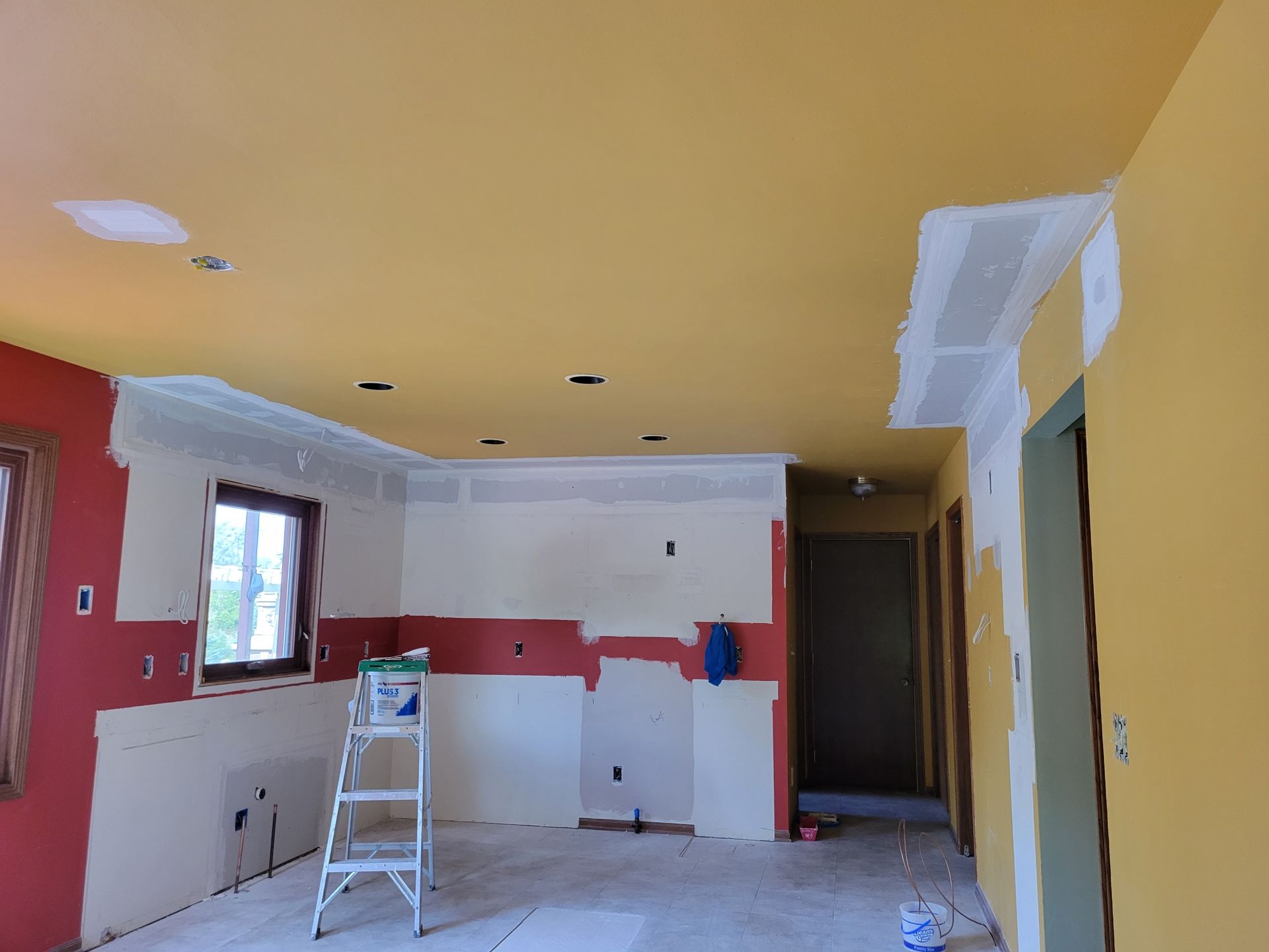 Partially renovated kitchen with yellow ceiling, red walls, and a step ladder on the floor