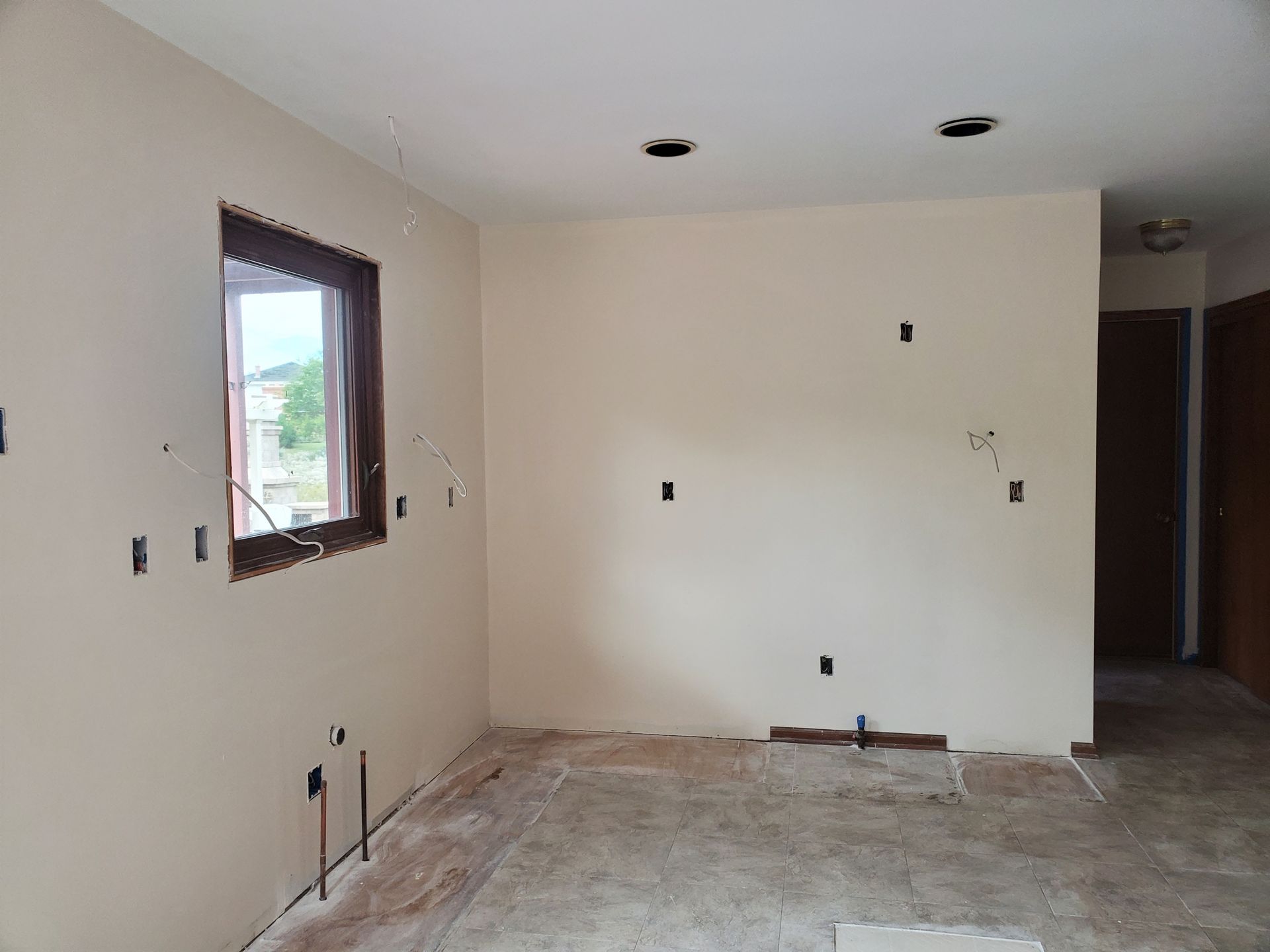 Empty unfinished room with bare walls, exposed outlets, a window, and unfinished concrete floor
