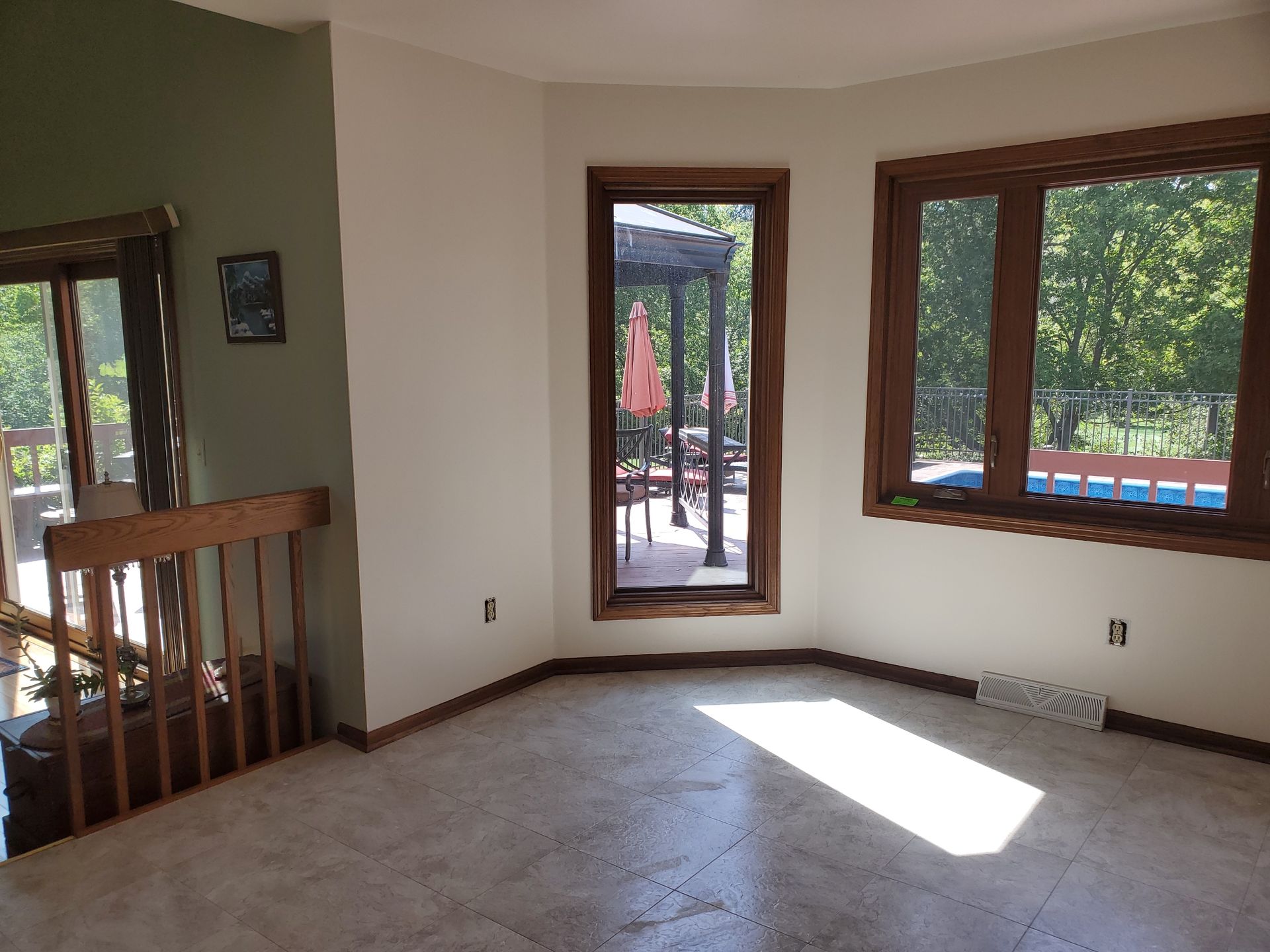 Empty living room with large windows and a sunlit floor, overlooking a patio and pool