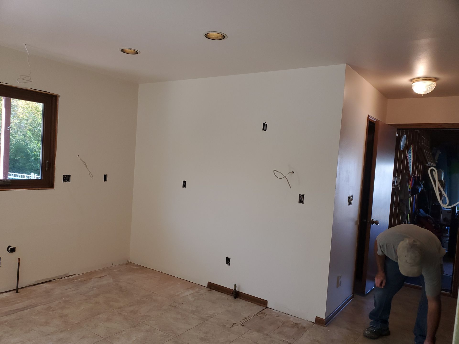 Empty room under renovation with white walls, bare floor, and a worker bending near the hallway.