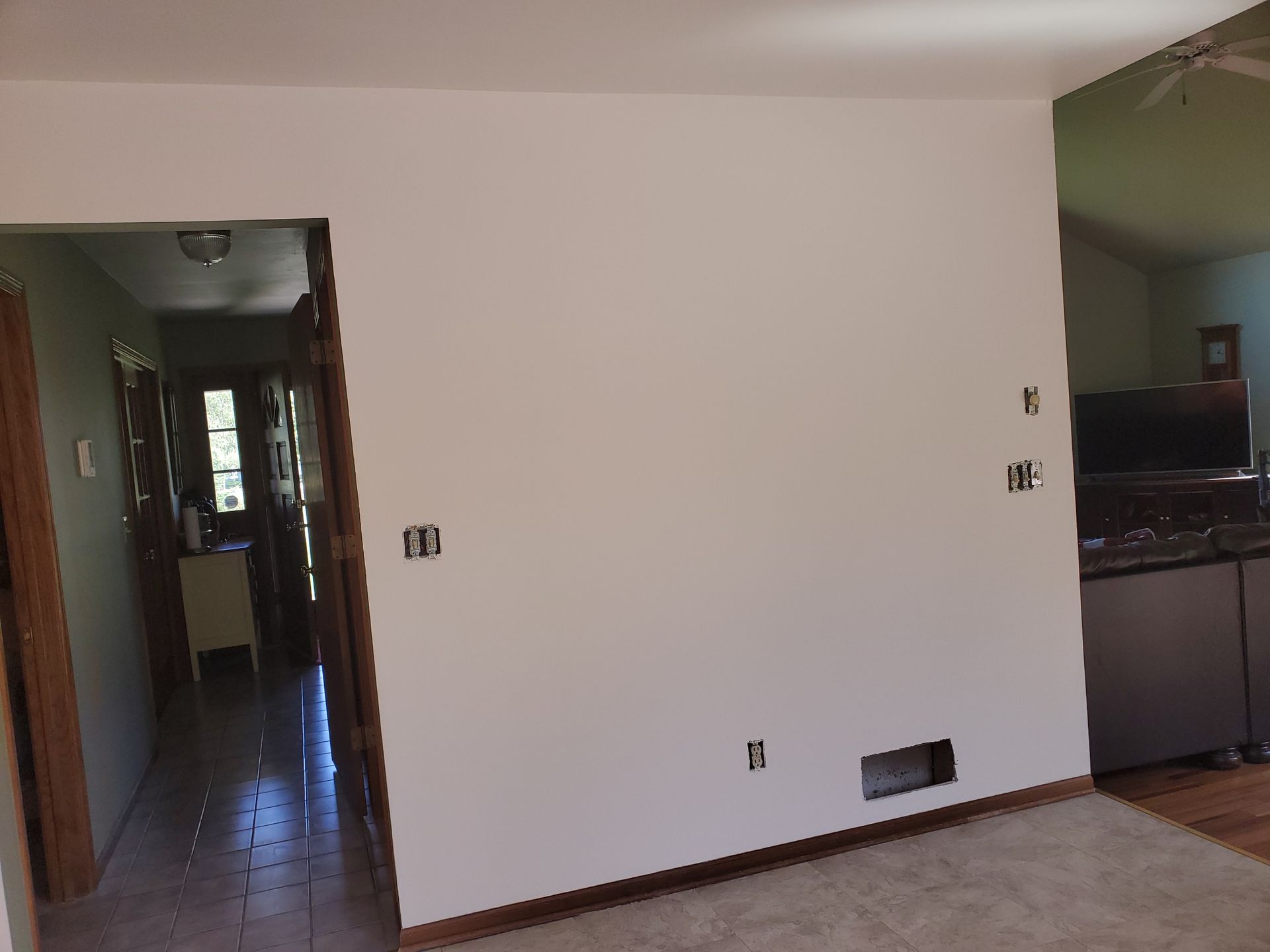 Empty white interior room with doorway to a hallway and a kitchen area on the right