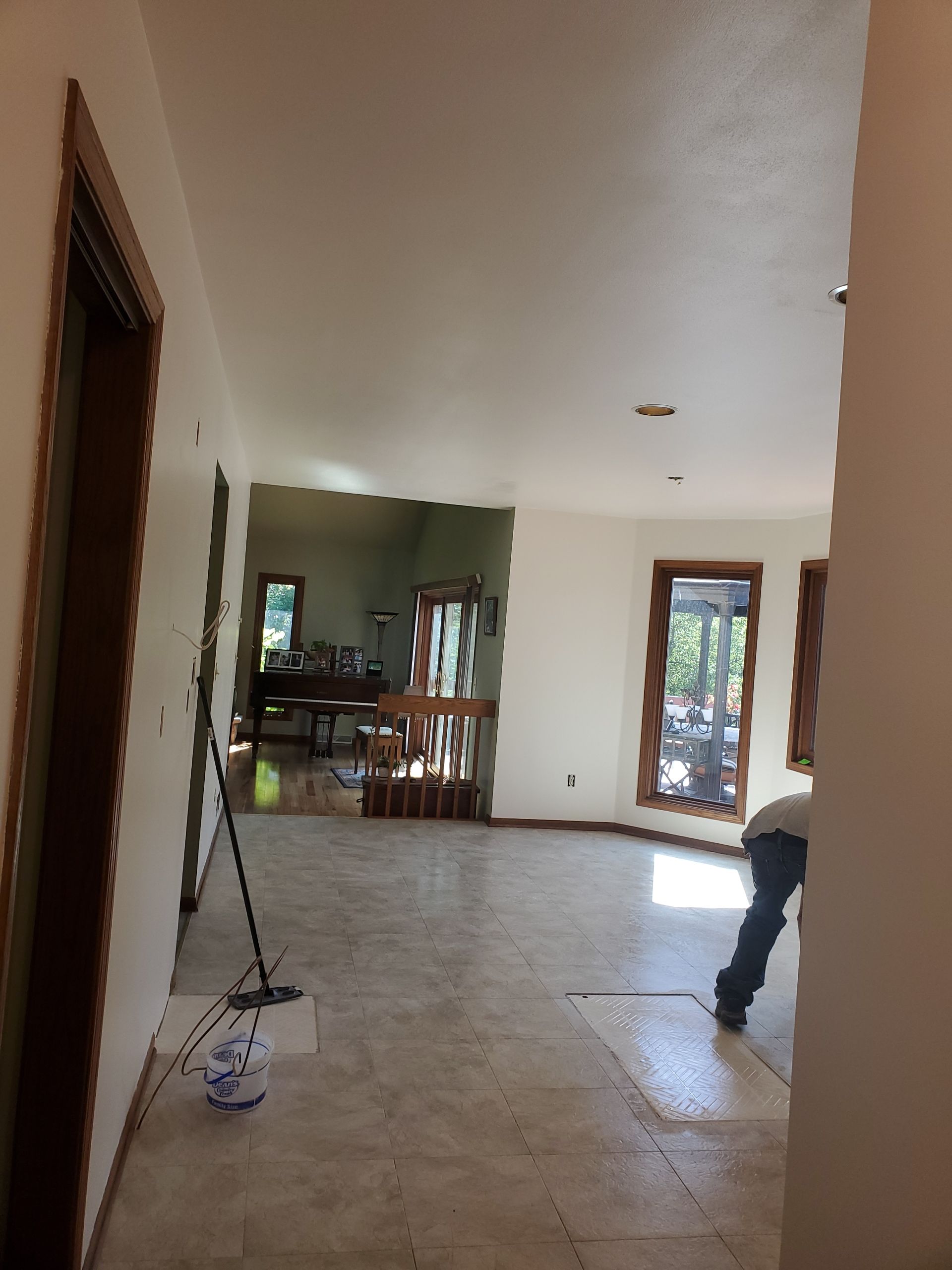 Empty tiled living room with open doorway, a mop on the floor, and a person partially visible at right