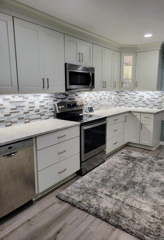Modern white kitchen with stainless steel appliances, gray tile backsplash, and a patterned rug