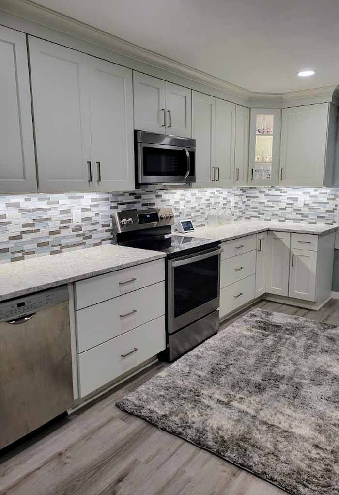 Modern white kitchen with stainless steel appliances, mosaic backsplash, and gray rug