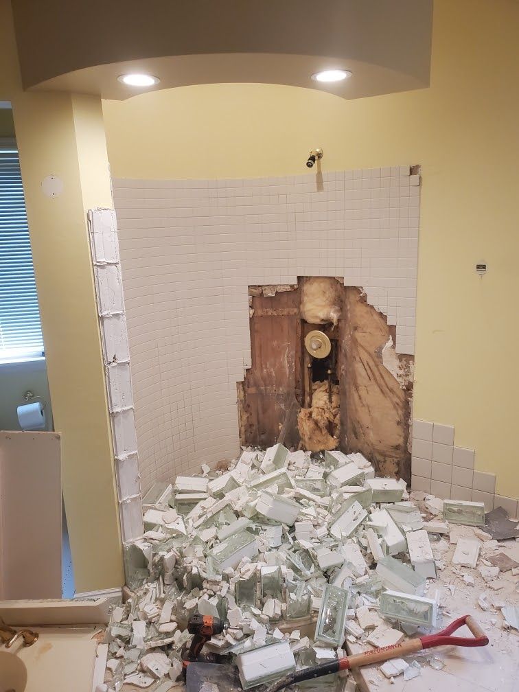 Bathroom wall demolished, with pile of broken tiles and debris on the floor.