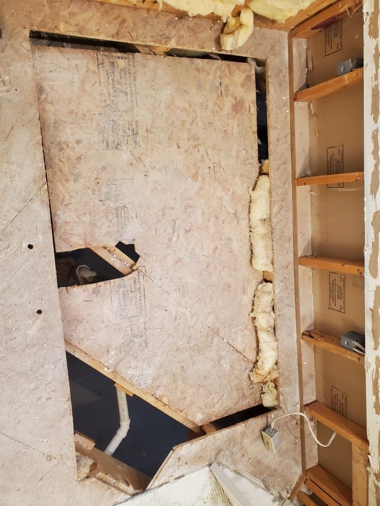 Damaged wall panel with a large hole, exposed insulation, and a shelving unit beside it