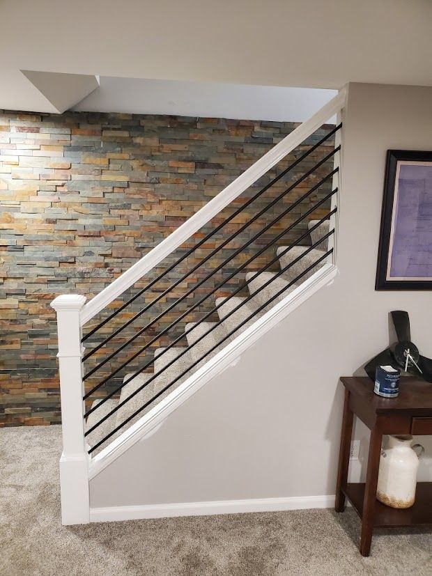 Staircase with white railing and black cable balusters beside a stone accent wall in an indoor hallway