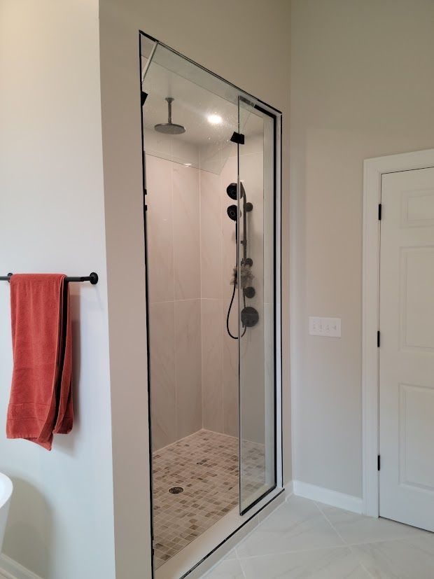 Bathroom shower with glass door, built-in shelf, and red towel on wall rack