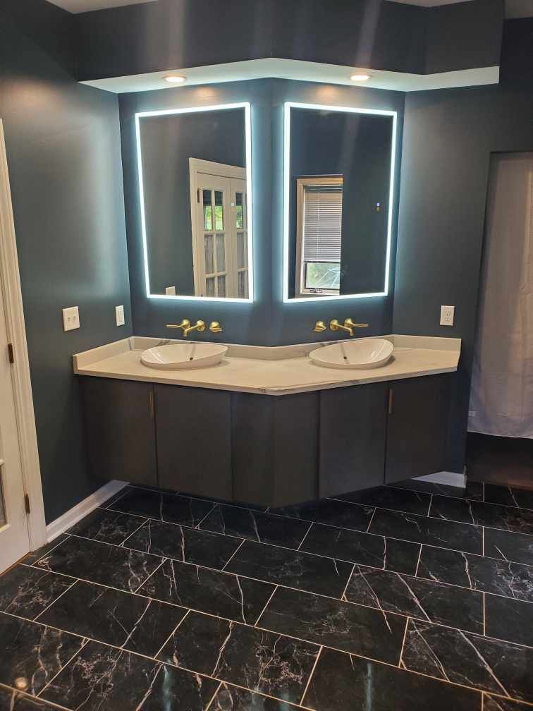 Dark restroom vanity with two sinks, illuminated mirrors, and black tile floor