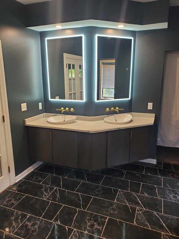 Modern bathroom vanity with double sinks, backlit mirrors, and dark tile flooring
