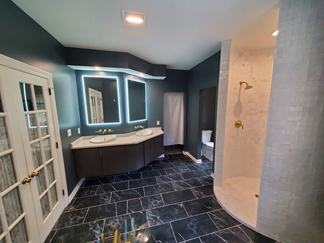Modern bathroom with dark tiled floor, double vanity, mirror lights, shower, and toilet.