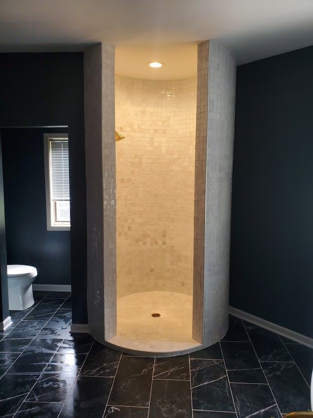 Modern bathroom with a curved tiled shower stall, black floor tiles, and dark walls